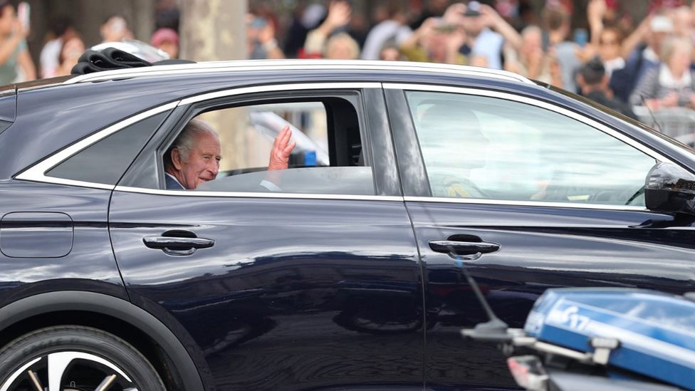 Король Чарльз машет рукой из машины, проезжая по Елисейским полям в Париже