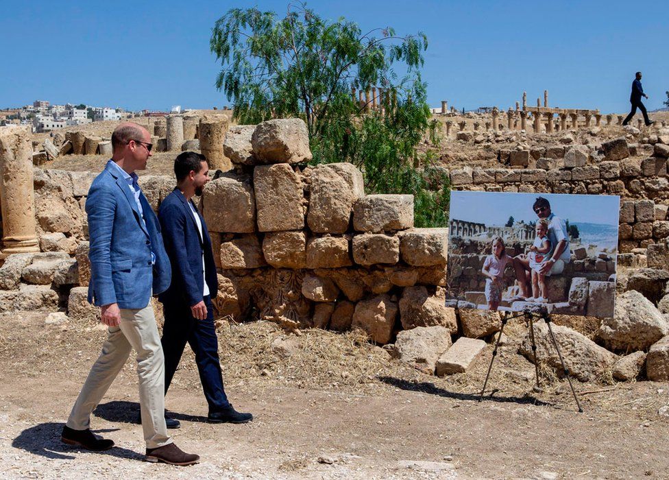 Prince William, Duke of Cambridge and Crown Prince Hussein of Jordan walk past an enlarged photo of Catherine, Duchess of Cambridge in her youth with her father on a family holiday