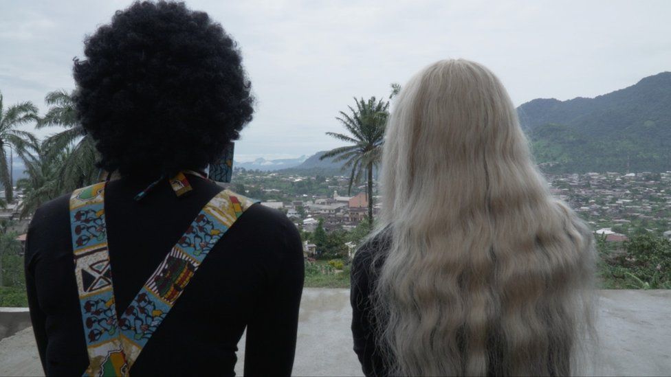 Две женщины, одна в афро, другая в светлом парике, смотрят на город спиной к камере