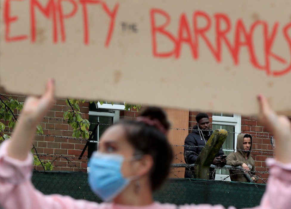 Asylum seekers watch a protest outside Napier Barracks