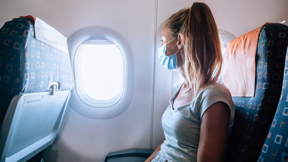 A woman sits in an aeroplane wearing a mask