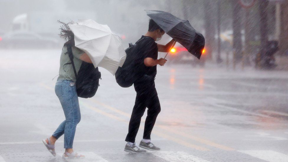 People struggle to hold onto their umbrellas in a crosswalk in the rain in Seoul, South Korea, 08 August 2022, as the rainy season revisits the country.