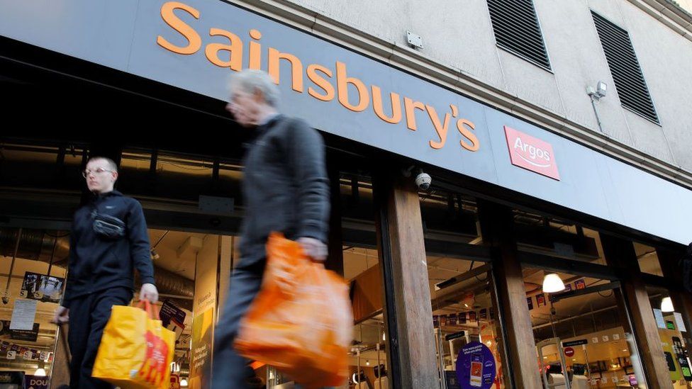 Two people walk past a Sainsbury's store