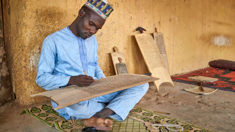 Мусульманин практикует кораническую каллиграфию на деревянной доске в Катсине, север Нигерии, 2019 г.
