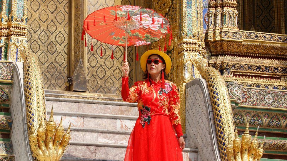 A Chinese tourist poses for a photo as they visit the Temple of the Emerald Buddha in Thailand.