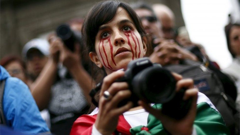 A woman with red paint on her face and a Mexican national flag takes part in a march in Mexico City. Photo: 26 September 2015