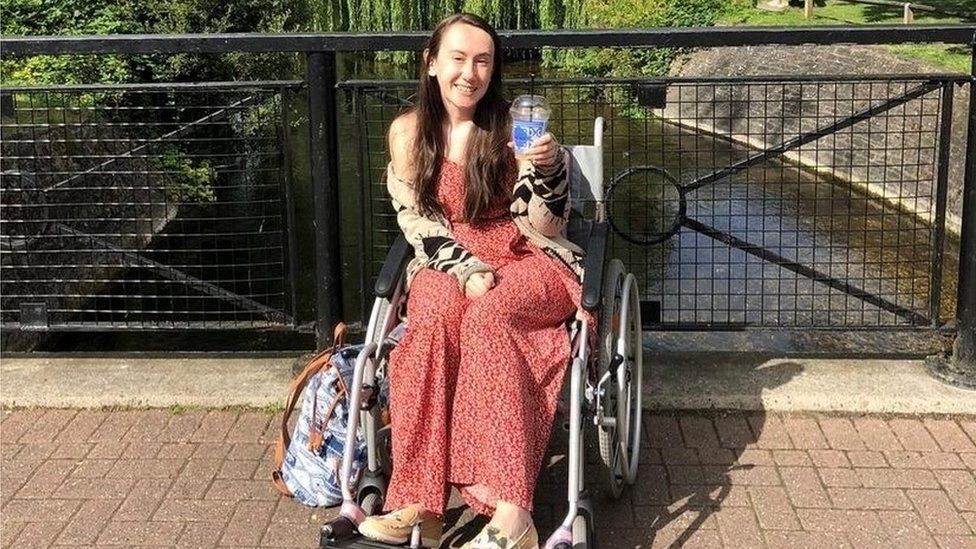 Cat Ray in her wheelchair. She is wearing a pink dress and holding a drink