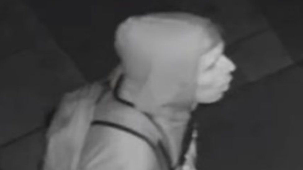 Black and white image showing a side profile of the suspect wearing a hoodie and backpack