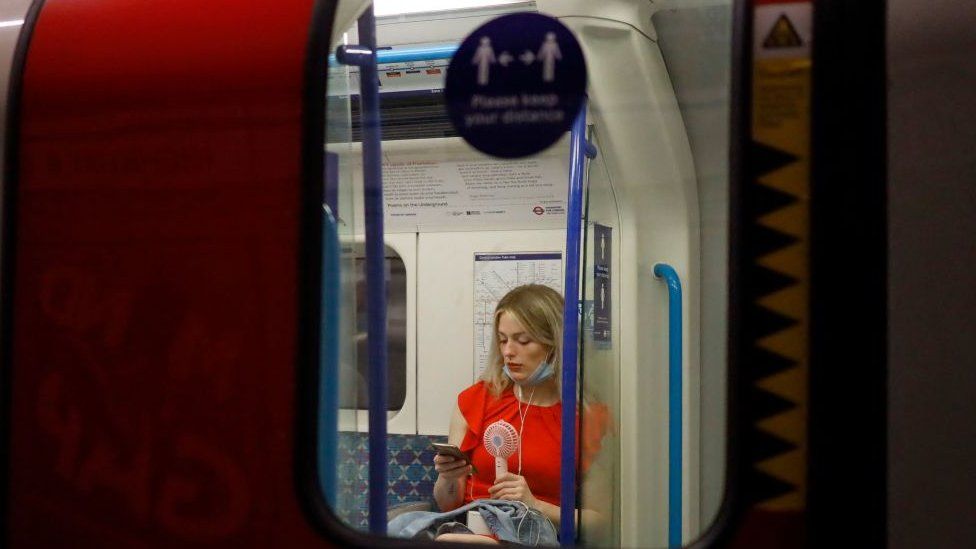 A woman fans herself with an electric fan on the tube in London