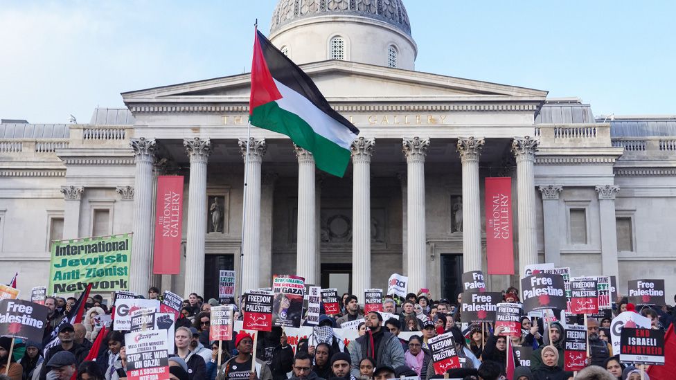 A large crowd gathers in Trafalgar Square holding Palestinian flags and placards