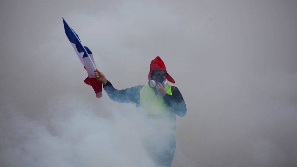 A demonstrator holds a French flag as he walks amid the tear gas during a protest of Yellow vests (Gilets jaunes) against rising oil prices and living costs, on December 1, 2018 in Paris