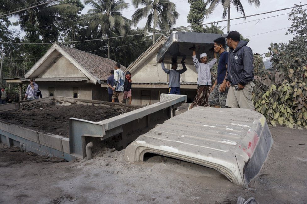 Villagers carry their belongings near a truck buried under ash from Mt Semeru at Sumber Wuluh village in Lumajang, East Java, Indonesia, on 5 December 2021.