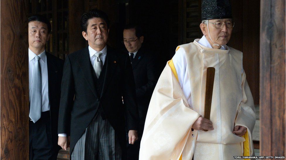 A Shinto priest (R) leads Japanese Prime Minister Shinzo Abe (C) as he visits the controversial Yasukuni war shrine in Tokyo on December 26, 2013,