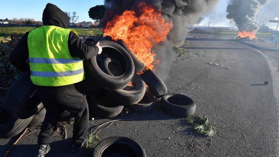 A man wearing a yellow vest burns tyres at a road blockade during a demonstration to protest against the rise in the price of oil and the cost of living, on December 11, 2018, in Aimargues, near Montpellier, southern France