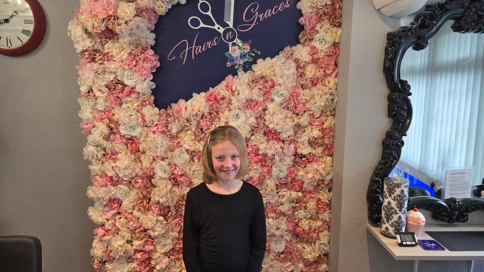 Lily-Mae after her charity haircut standing in front of a flower wall