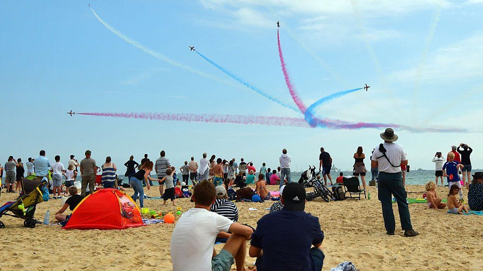 People look on from the beach as the Red Arrows aerobatics display team perform during the Bournemouth Air Festival on August 18, 2016