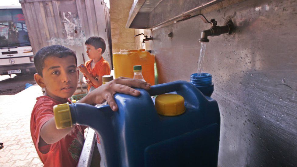 A Palestinian boy pours water into a container from a desalination plant