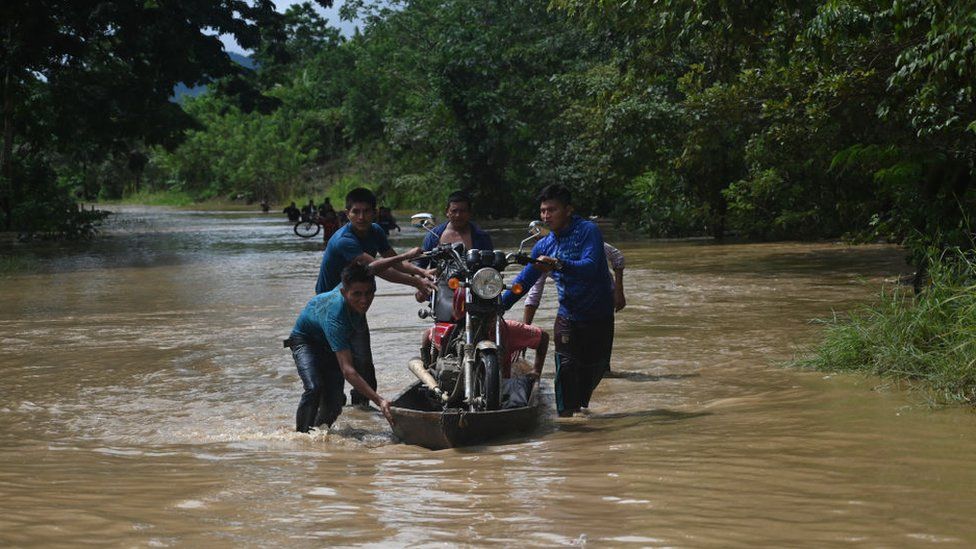 People carry a motorbicycle on a boat in a flooded area in Panzos, Alta Verapaz