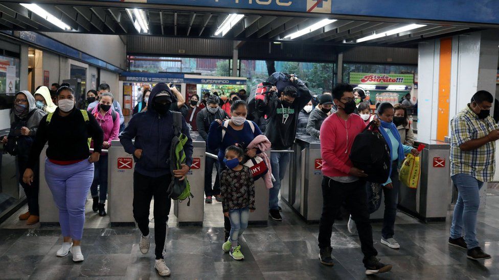 People wearing protective masks walk past the turnstiles inside a subway station in Mexico City