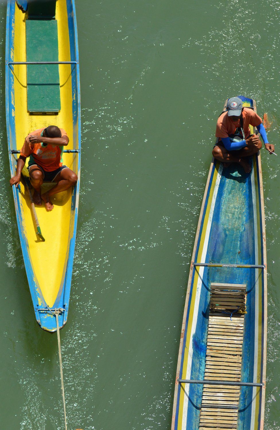 Two men sit in brightly painted canoe boats
