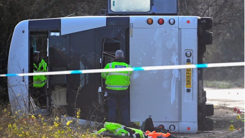 Close up of overturned bus with two officers in high vis stood near it