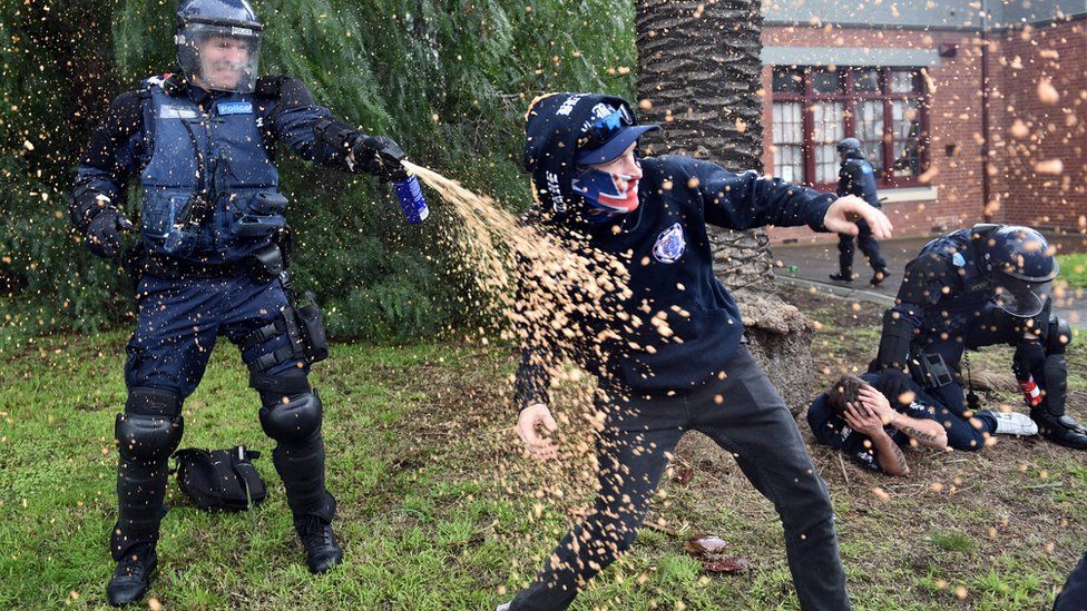 A policeman uses pepper spray towards a protester during clashes in the Melbourne suburb of Coburg, Australia, 28 May 28.