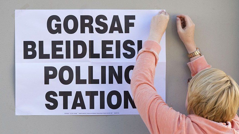 Woman pinning polling station poster up in Welsh language and English