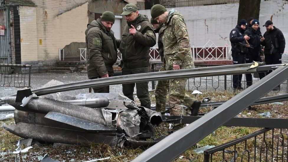Police and security personnel inspect the remains of a shell in a street in Kyiv on February 24, 2022.
