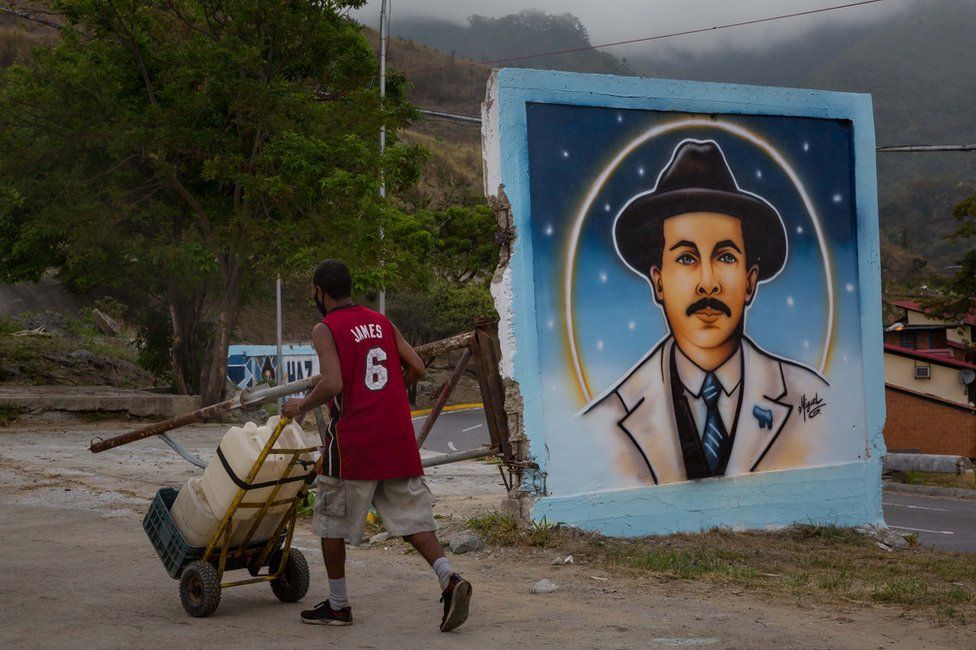 Мужчина толкает тележку у фрески с изображением Хосе Грегорио Эрнандеса в Каракасе