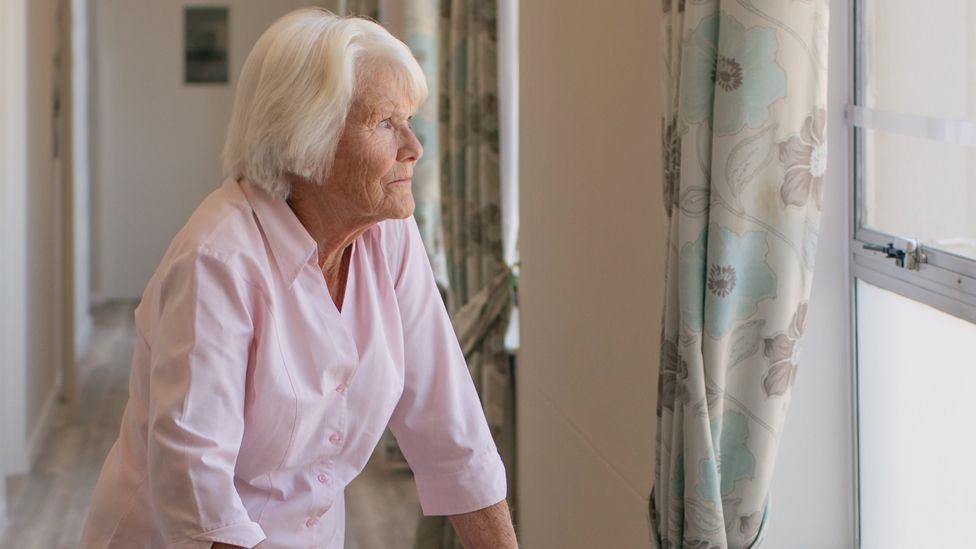 Stock image of an elderly woman looking out of the window in a corridor of a care home