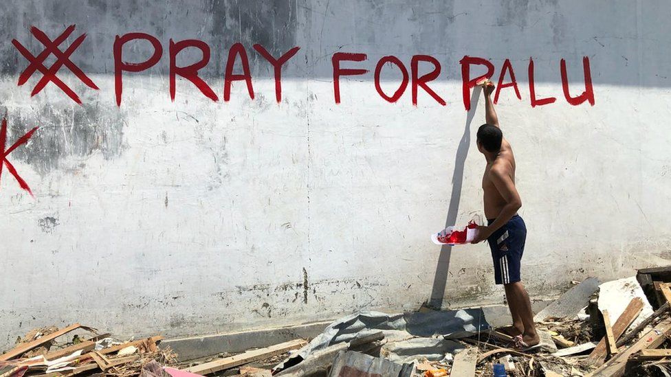 A man paints the words Pray for Palu on a wall in Palu