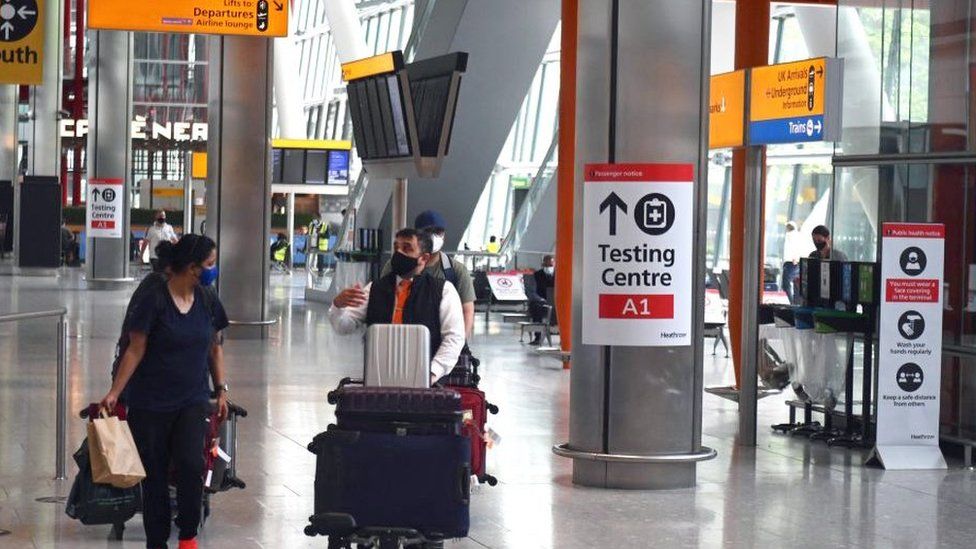 Passengers push their luggage past signage displaying the way to a Covid-19 test centre, in Terminal 5 at Heathrow airport in London,
