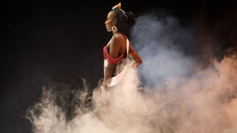 A woman walking the runway, surrounded by smoke. The background the is black.