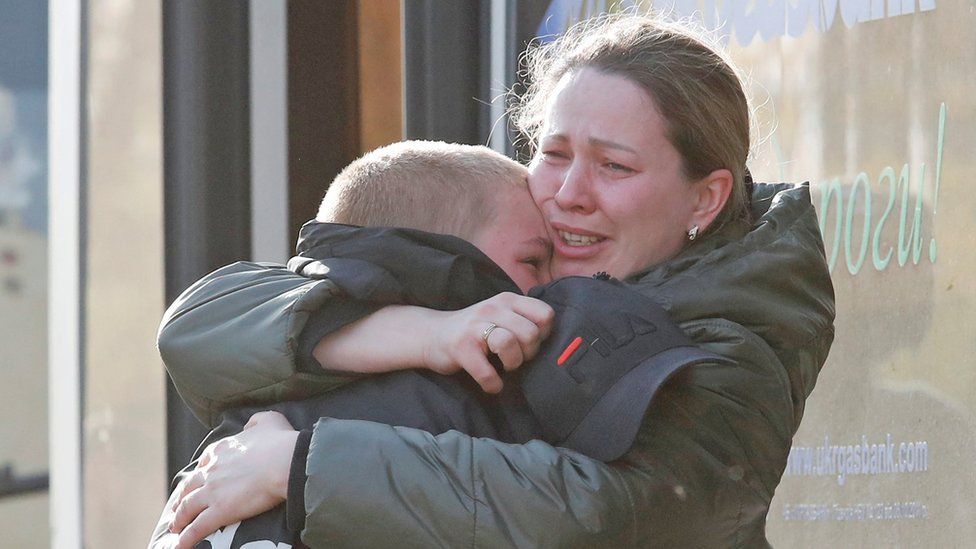 A tearful woman and son embrace next to a bus in Bezimenne