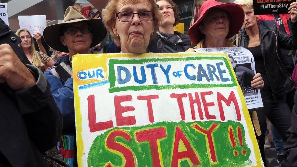 A woman protesting Australia's offshore detention policy holds a placard saying "Our duty of care: let them stay"