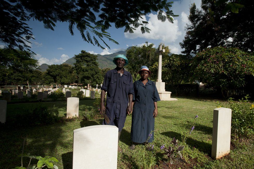 Shadrack Paull and Lusia Axalte stand holding hands among the graves at the cemetery in Tanzania