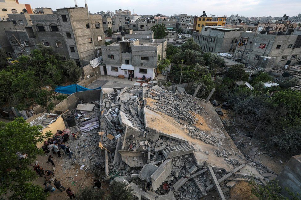 Palestinians from the Nabhan family gather near the rubble of their destroyed family house following an Israeli air strike in Jabaliya, in the northern Gaza Strip (14 May 2023)