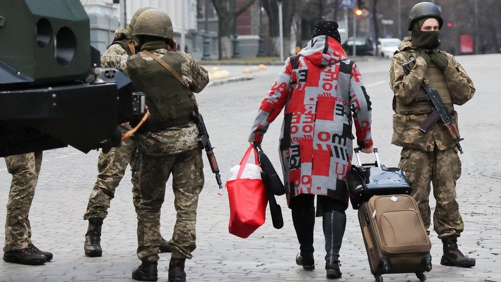 A woman walks past Ukrainian military service members guarding a road