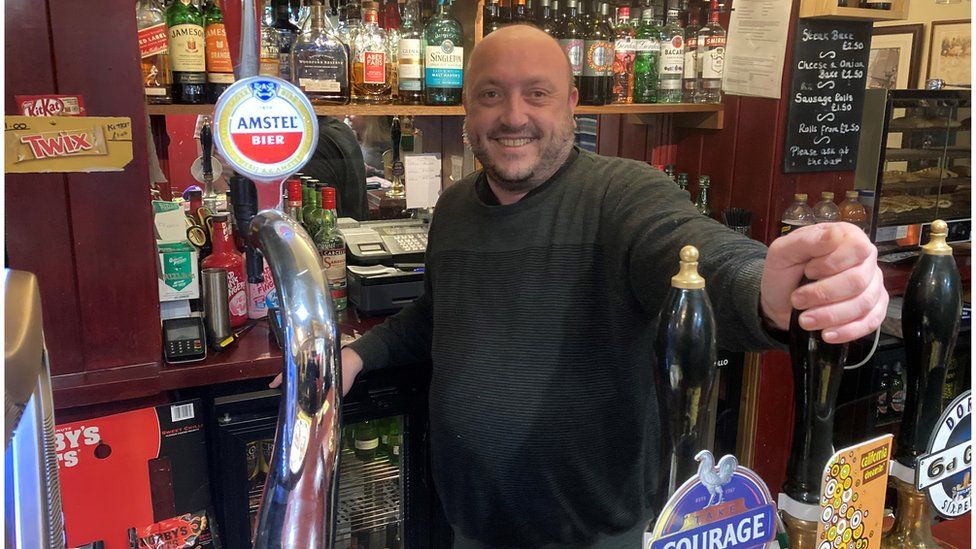 Pub manager, Paul Cooper, smiling behind the bar