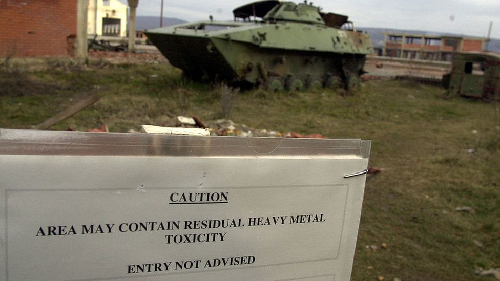 Destroyed armoured vehicles in Kosovo, 1999, and sign warning of heavy metal toxicity