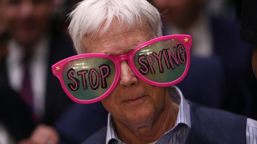 a protester in a pair of oversized glasses emblazoned with the words "stop spying"