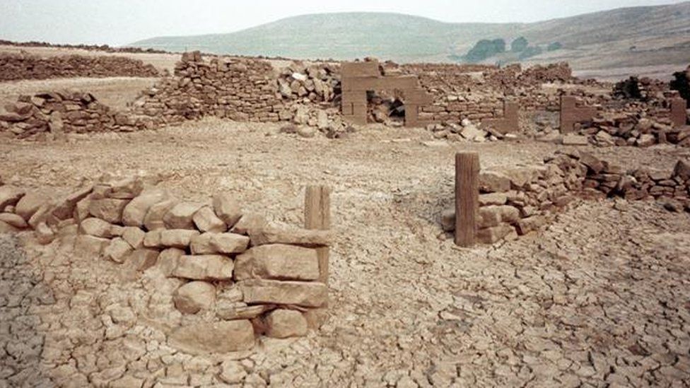 The stone remains of the village in front of a mountain backdrop.