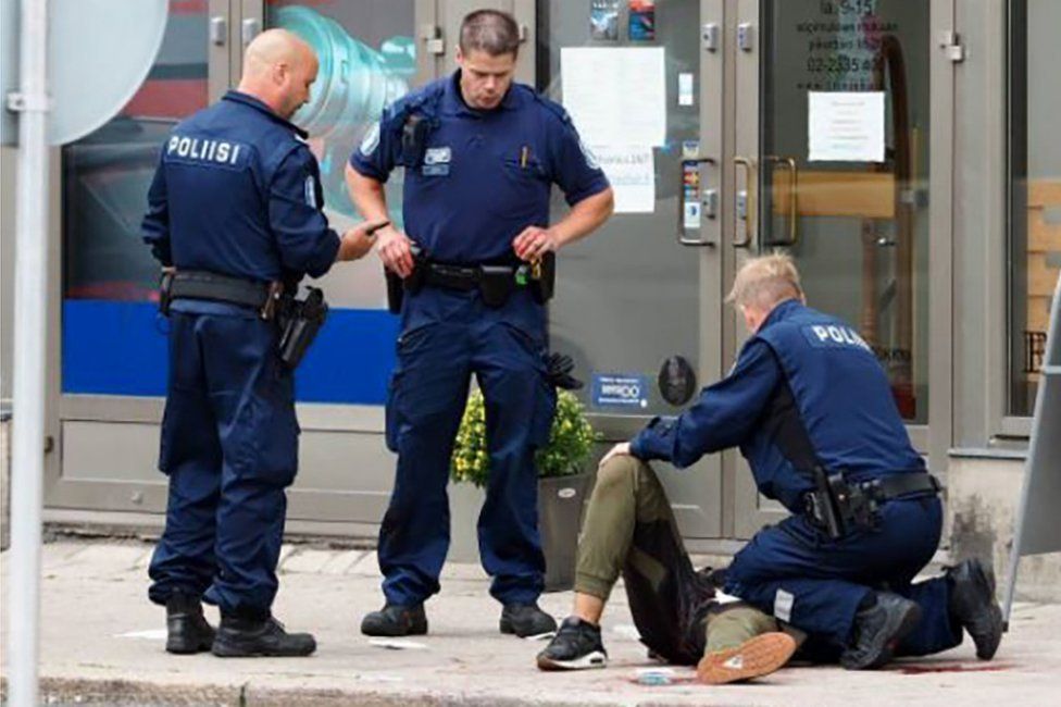 Three armed Finnish police officers tend to a man lying on the pavement at the scene