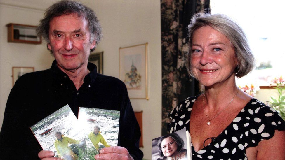 Tony James pictured with Kate Adie, another journalist. They are stood side by side, looking at the camera and smiling. They are both holding books which they have written.