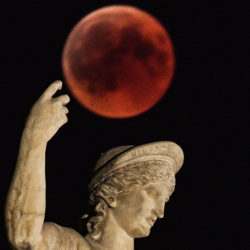 A picture shows the full moon during a 'blood moon' eclipse beside a statue of ancient Greek god Ares in central Athens on July 27, 2018