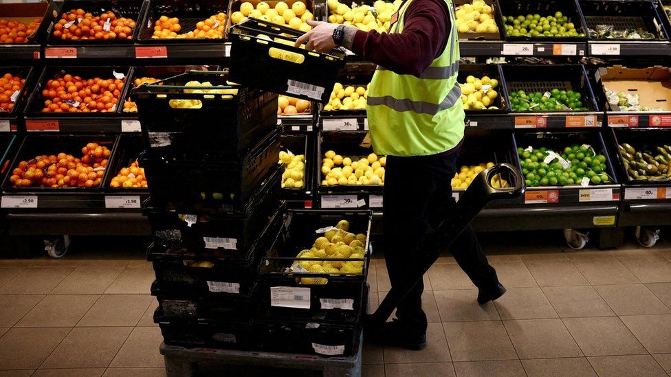 A supermarket worker stacks crates of fruit in a Sainsbury's in Richmond, west London.
