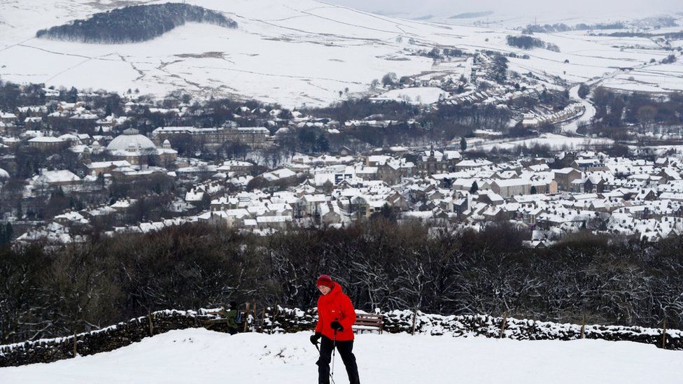 Man hiking up snowy hill with snow covered Buston in the background