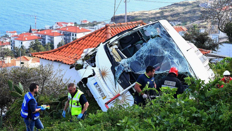 Firemen stand next to the wreckage of a tourist bus that crashed in Madeira on April 17, 2019