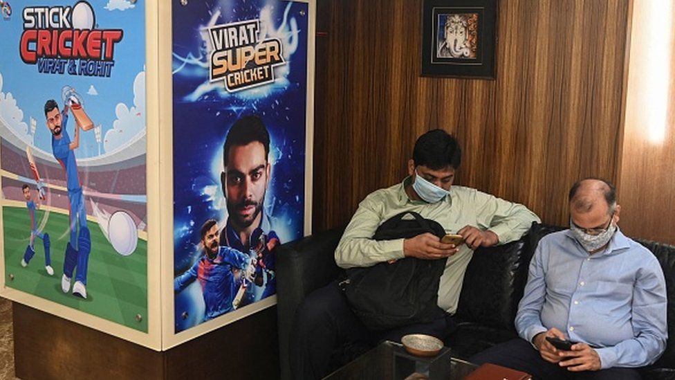 A visitor sits next to a poster featuring Indian cricketers Virat Kohli and Rohit Sharma (L) at the reception area of Nazara Technologies Ltd., the country's top mobile cricket gaming app maker, in Mumbai on March 19, 2021.