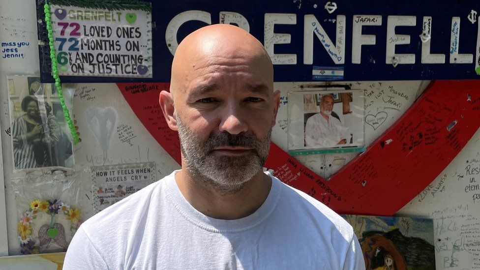 Marcio Gomes in front of the Grenfell memorial wall in 2023